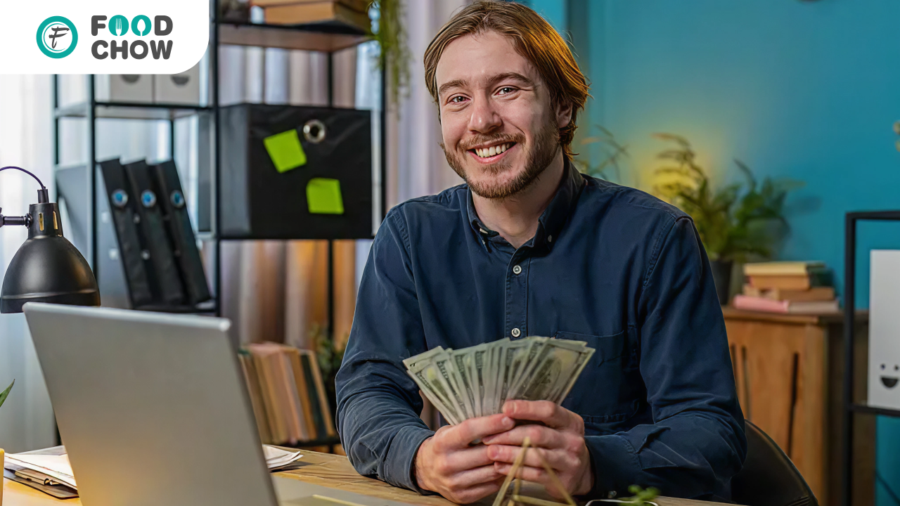 FoodChow partner in the UK working on a laptop and holding cash, representing recurring income opportunities through restaurant software reselling.